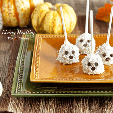 halloween dessert ghost truffles with chocolate chip eyes and decretive pumpkins in the background