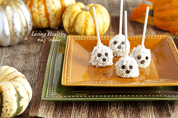 halloween dessert ghost truffles with chocolate chip eyes and decretive pumpkins in the background