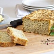 loaf of paleo pesto cheese bread with two slices cut on a cutting board with knife and plates in background