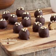 wooden cutting board with numerous paleo peanut butter truffles topped with small pieces of nuts