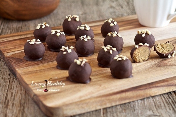 wooden cutting board with numerous paleo peanut butter truffles topped with small pieces of nuts