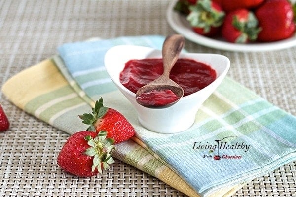 serving dished filled with homemade sugar free strawberry jam with wooden spoon on top and strawberries on side and behind 