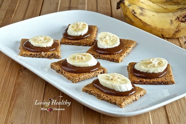 white plate with six paleo graham crackers topped with homemade nutella and a slice of banana and two bananas in background 