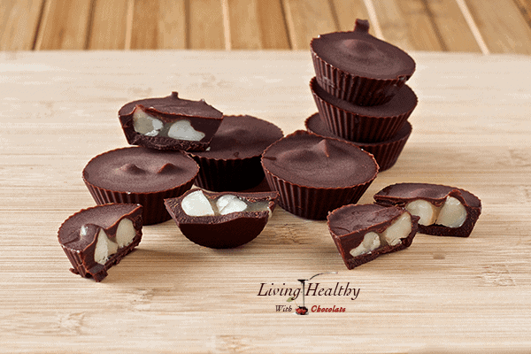 wooden table topped with several chocolate caramel macadamia nut cups with several cut in half 
