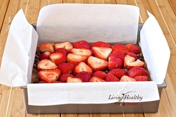 square baking pan lined with parchment paper with paleo chocolate strawberry crumble dessert topped with cut strawberries 