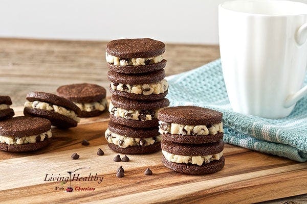 stacks of homemade paleo cookie dough Oreos on wooden table with glass of milk in background