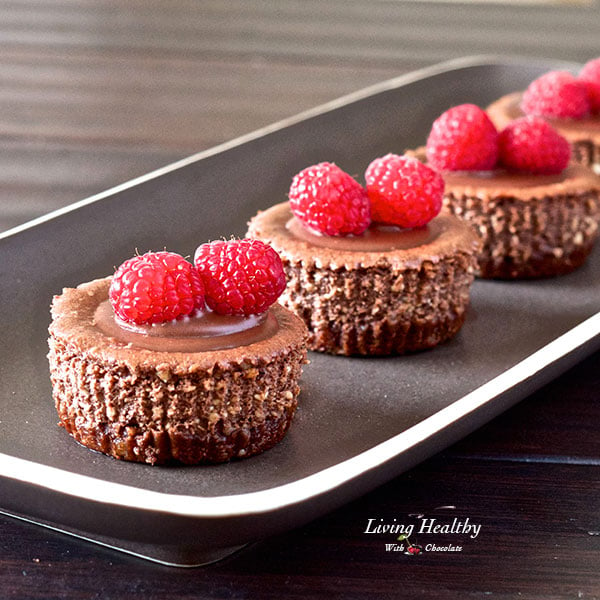 plate of four mini chocolate cheesecakes topped with raspberries 