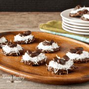 wooden serving tray with six no bake cookies topped with coconut and a stack of plates with more cookies in background