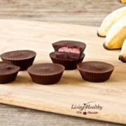 wooden cutting board with numerous strawberry banana chocolate cups and bananas in the background