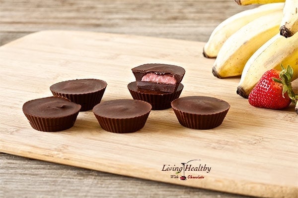 wooden cutting board with numerous strawberry banana chocolate cups and bananas in the background 