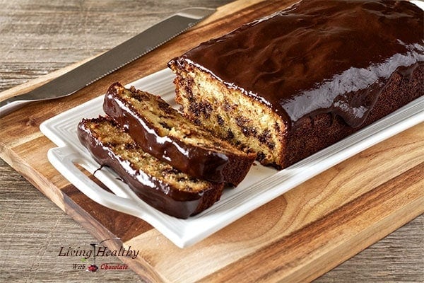 loaf of paleo chocolate chip bread with two slices cut out on a white plate with knife to the left