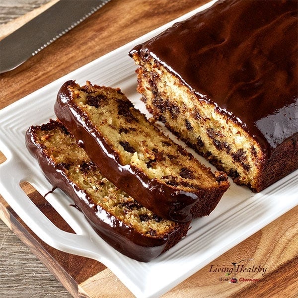 loaf of paleo chocolate chip bread with two slices cut out on a white plate with knife to the left