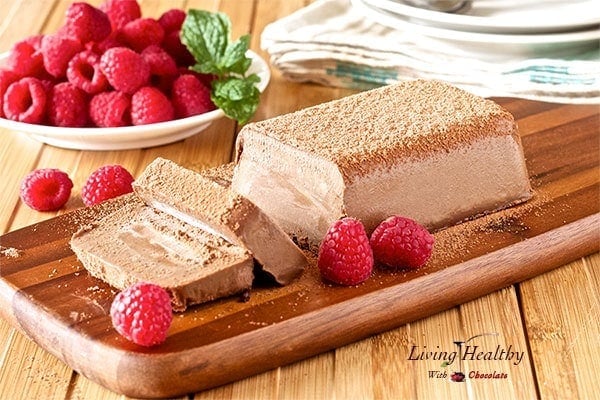 a wooden cutting board with paleo chocolate expresso fudge and raspberries in a plate in background