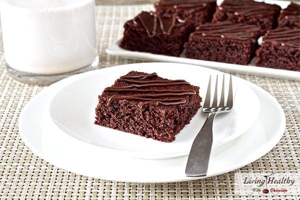 square piece of chewy fudgy chocolate brownie on plate with fork and glass of milk with more squares in background 