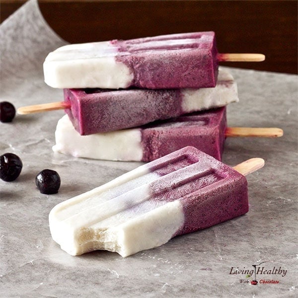 four blueberry vanilla yogurt popsicles on parchment paper with a few loose blueberries to the left
