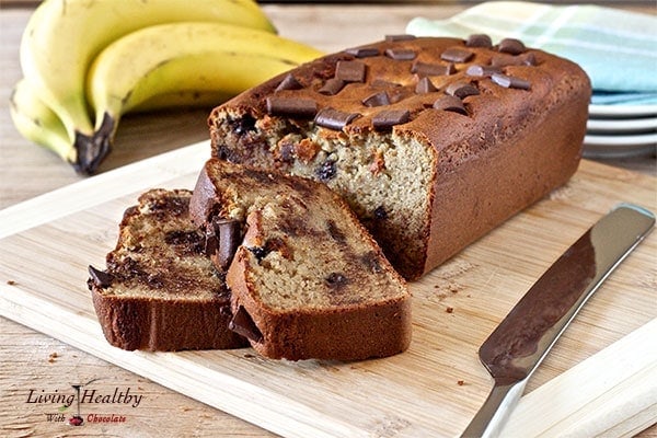 loaf of peanut butter cup banana bread with two slices cut and bananas in background