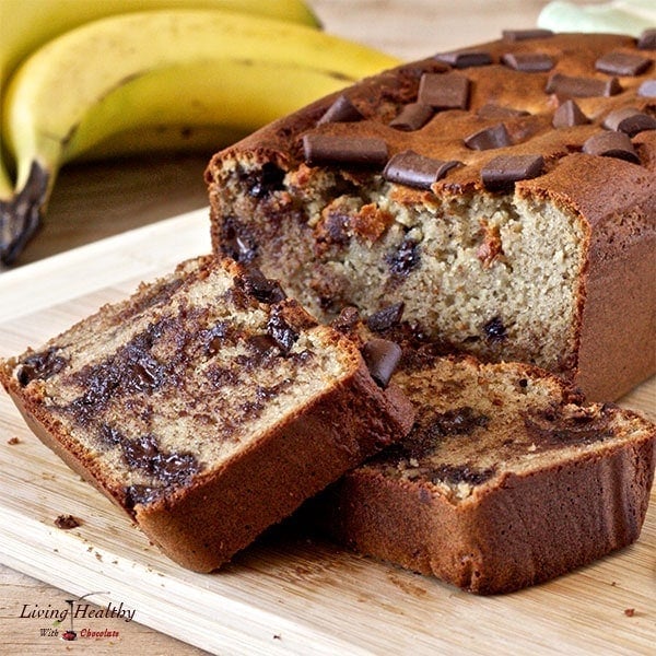 close up of loaf of peanut butter cup banana bread with two slices cut and bananas in background