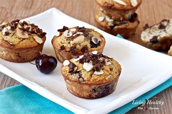 three cherry muffins on a plate topped with chocolate chunks and sliced almonds