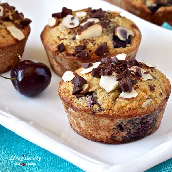 close up of two cherry muffins topped with chocolate chunks and sliced almonds on a white plate