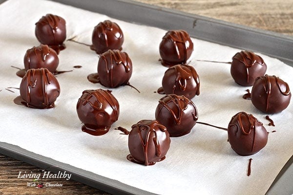 Carrot cake truffles drizzled in chocolate sitting on parchment paper