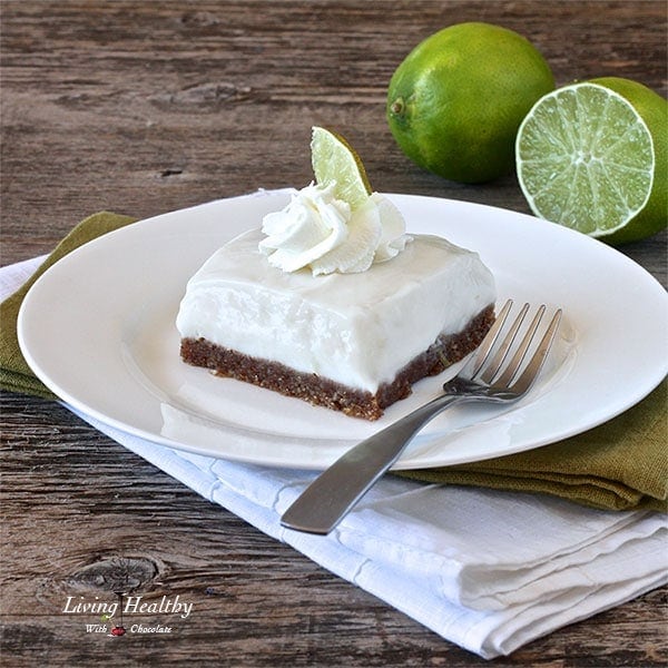 square piece of paleo key lime pie on white plate with fork and two limes in background 