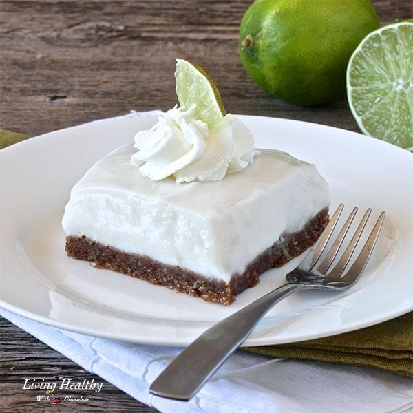 close up of a square piece of paleo key lime pie on white plate with fork and two limes in background 