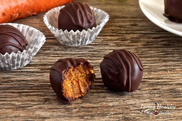 four carrot cake truffles on a wooden table with a bite taken off