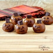 Halloween almond butter pumpkin truffle heads with spooky faces on a wooden table with colorful napkins in background