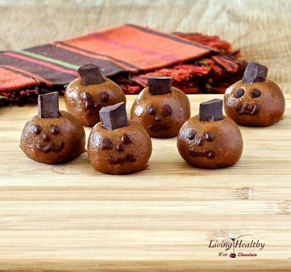 Halloween almond butter pumpkin truffle heads with spooky faces on a wooden table with colorful napkins in background 