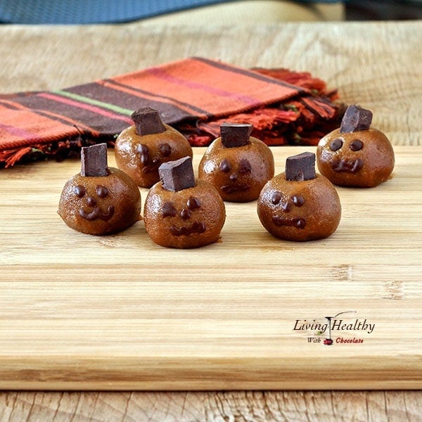 Halloween almond butter pumpkin truffle heads with spooky faces on a wooden table with colorful napkins in background 