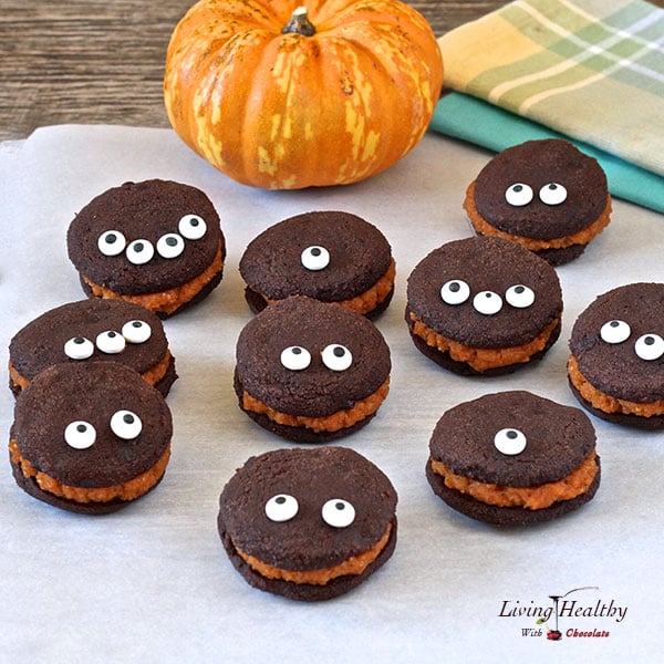 assortment of halloween chocolate whoopie pie cookies with pumpkin filling with funny eyes and small pumpkin in background 