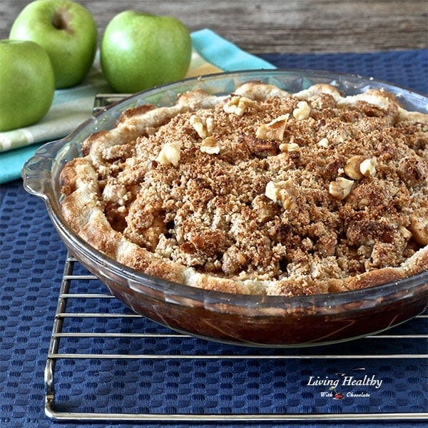 large apple pie cooling on a wire rack on top of blue place mat with three large green apples