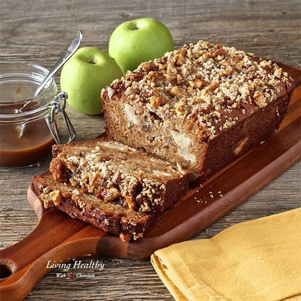 loaf of caramel apple pie bread on wooden cutting board with jar of caramel and two green apples in background