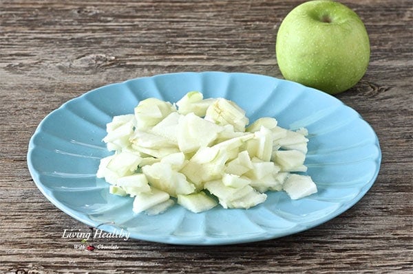 plate of cut up green apple on wooden table with one green apple in background 