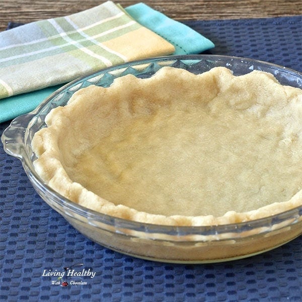 glass pie dish with empty pie crust sitting on blue place mat with colorful napkins in background 