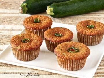 plate of five zucchini muffins on a brown and white place mat with two large zucchini in the background