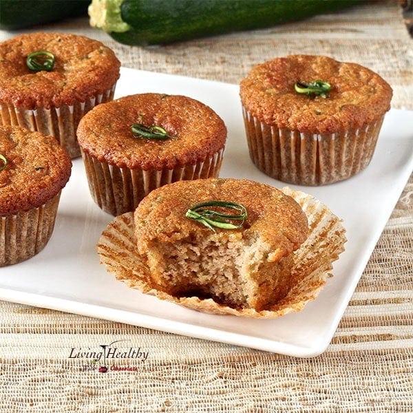 five zucchini muffins on a white plate and one muffins with a bite taken off