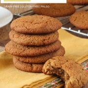 stack of paleo ginger cookies on yellow napkin and one with bite taken out with more cookies in background on cooling rack