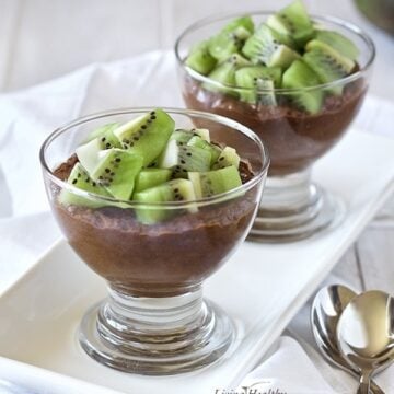 two glass serving bowls on a white plate filled with chocolate avocado pudding topped with chunks of kiwi