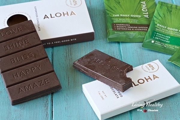 bars of Aloha chocolate sitting on a blue wooden table with wrappers and one bite taken out of one bar of chocolate