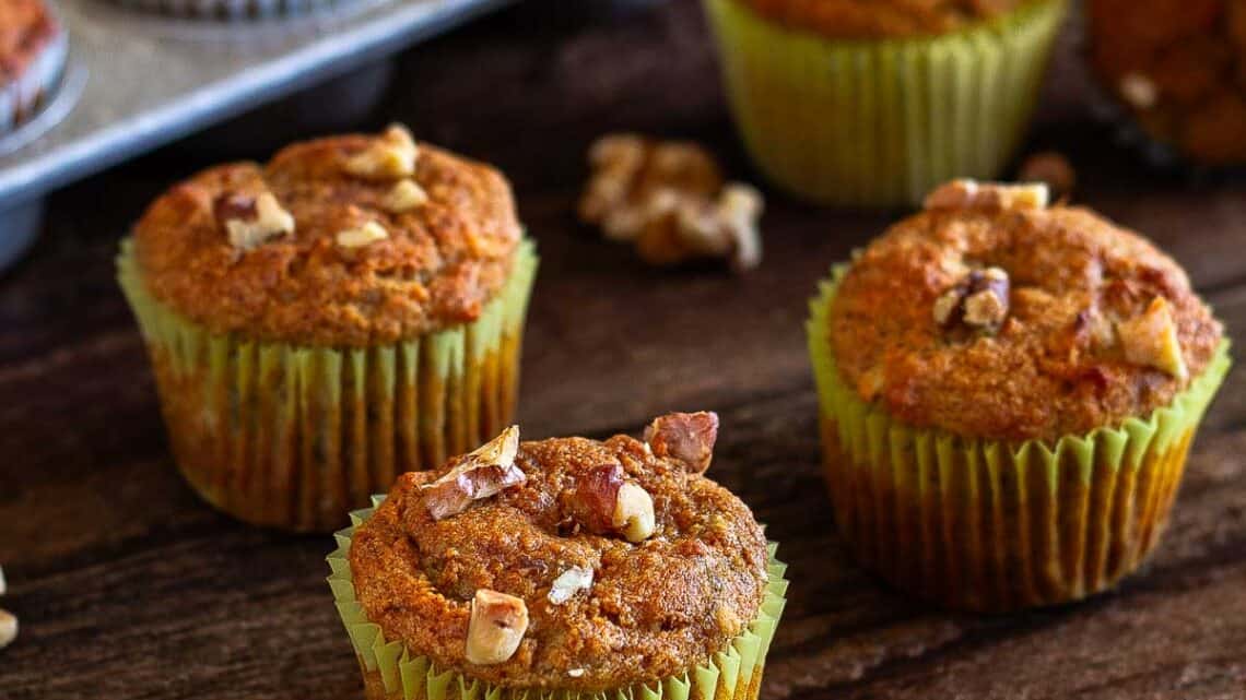 banana walnut muffins on a wooden table with a muffin pan in background filled with muffins