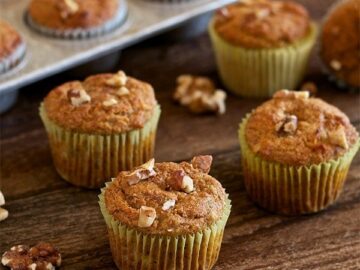 banana walnut muffins on a wooden table with a muffin pan in background filled with muffins