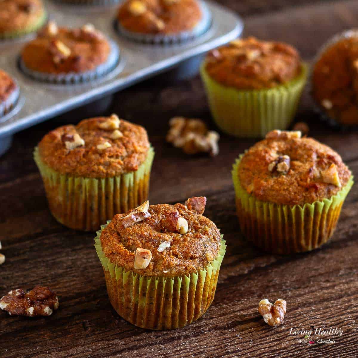 banana walnut muffins on a wooden table with a muffin pan in background filled with muffins