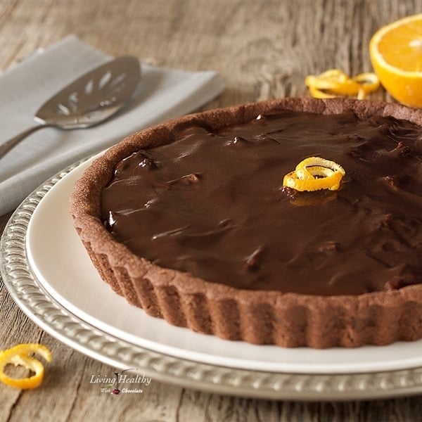 chocolate orange almond tart on a serving plate with orange spirit orange peel and half of an orange in background