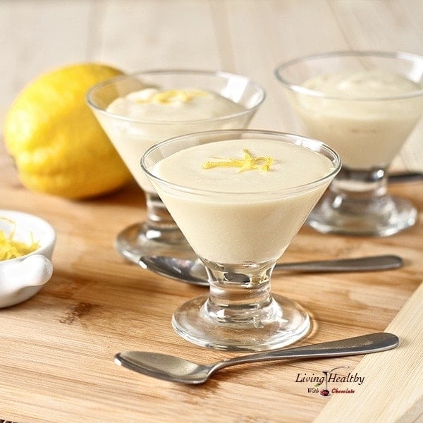 three glass serving cups with frozen white chocolate lemon mousse sitting on wooden board with spoons and a full lemon behind