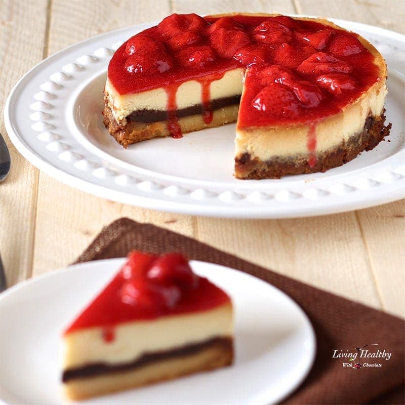 a large white chocolate strawberry cheesecake on a serving plate with one slice on separate plate in foreground