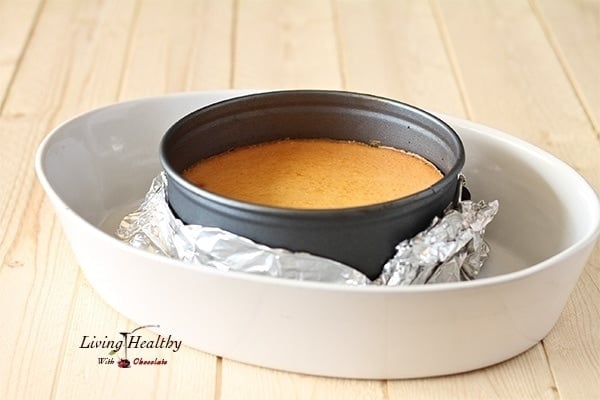 cheesecake base sitting in a round pie dish wrapped in foil resting inside a larger white dish 