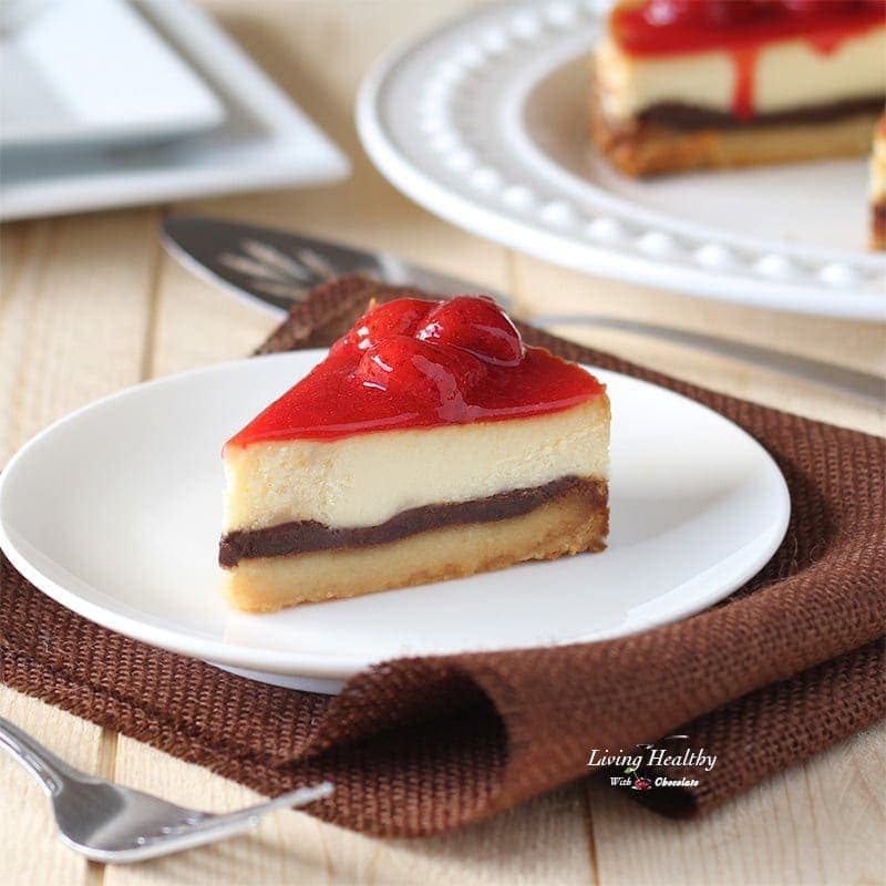 a slice of white chocolate strawberry cheesecake on a white plate with a full cake in the background