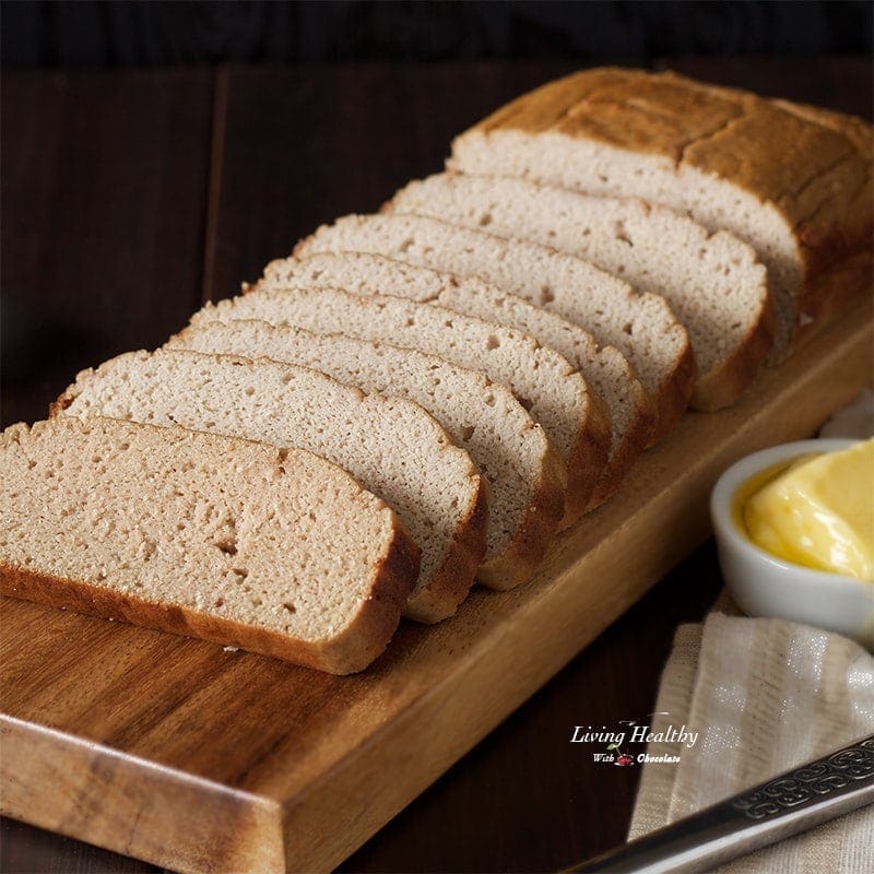 loaf of paleo sweet bread sliced into numerous pieces on wooden cutting board with dish of butter and knife