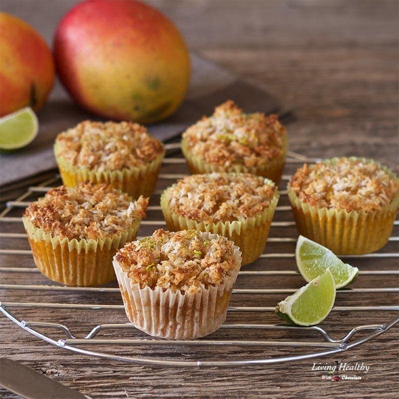 mango muffins topped with coconut lime streusel cooling on a round rack with lime wedges and mangos in background